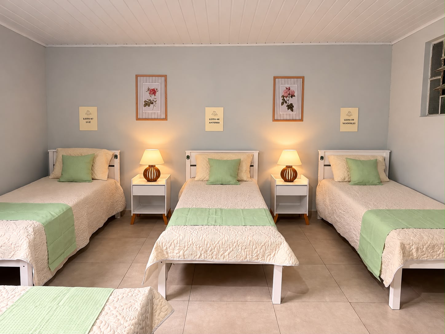 Quarto compartilhado claro com três leitos, abajures e quadros de rosas
