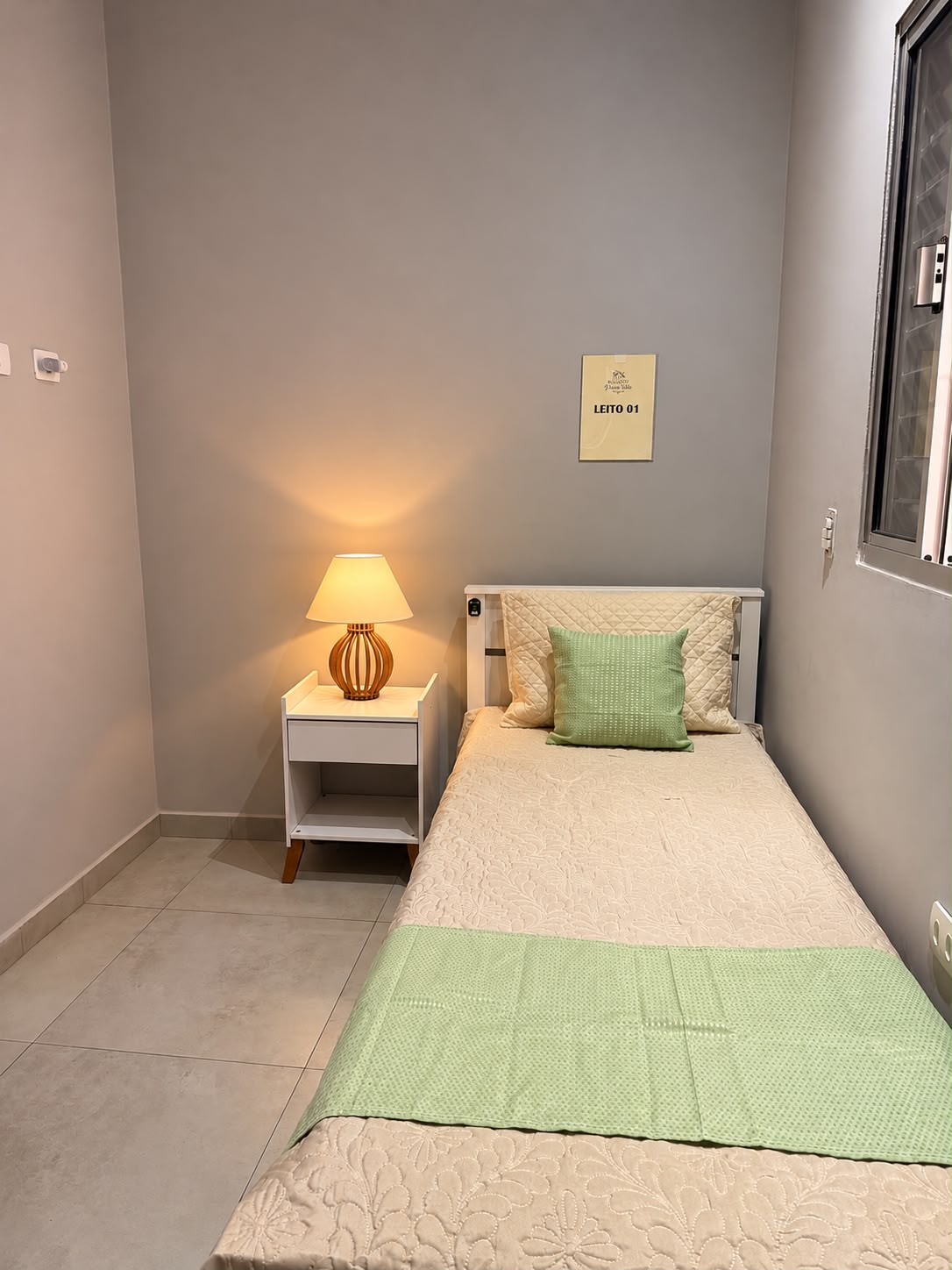 Quarto individual claro com leito numerado e abajur aceso
