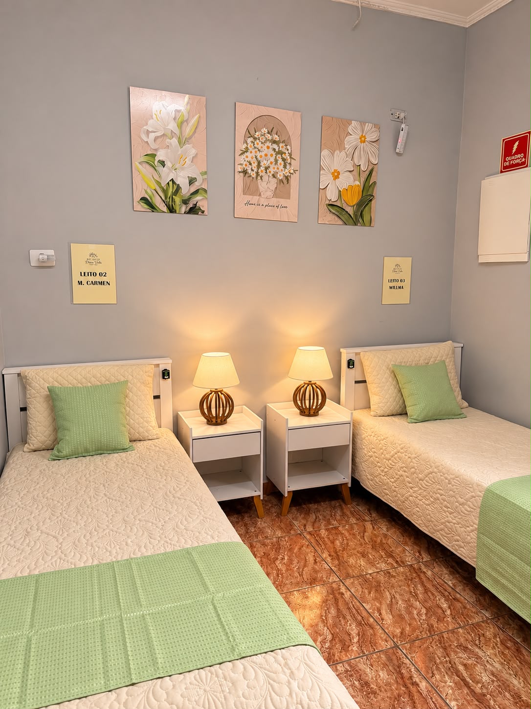 Quarto compartilhado com dois leitos, abajures e quadros de flores